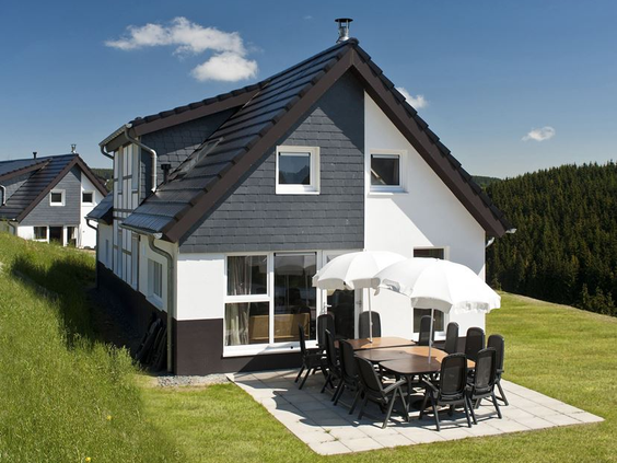 De buitenkant van een modern vakantiehuis bij Landal Winterberg in Sauerland, met een ruim terras en tuinmeubilair op een zonnige dag.