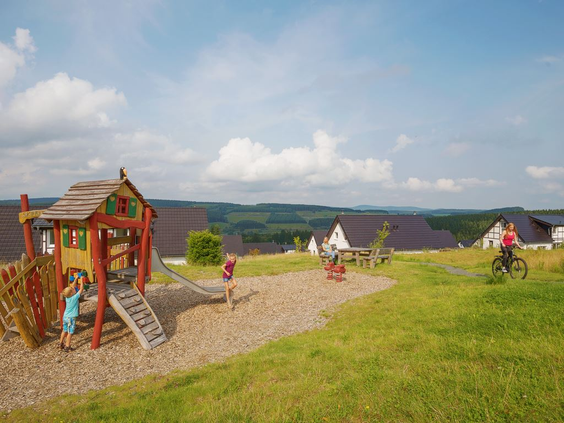 Kinderen spelen op de houten klimtoestellen in de buitenspeeltuin van Landal Winterberg, met uitzicht over het heuvelachtige landschap.