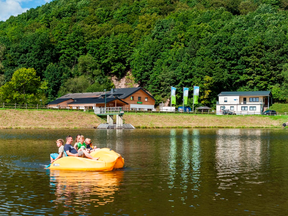 Een gezin heeft plezier op een gele waterfiets op het recreatiemeer van Landal Wirfttal, omringd door de groene heuvels van de Eifel.