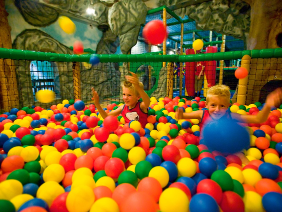 Kinderen hebben plezier en spelen in de grote ballenbak vol gekleurde ballen in de binnenspeeltuin van Landal Wirfttal.