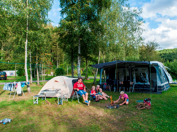 Een gezin geniet van het kamperen op een ruime kampeerplaats met caravan en tent op Landal Wirfttal.