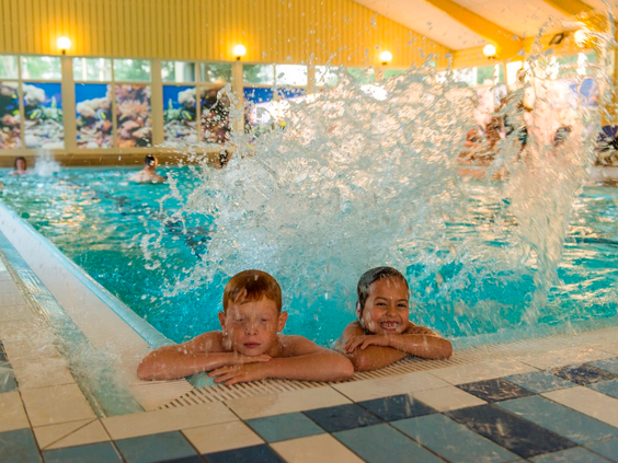 Twee jongens lachen en spetteren in het binnenzwembad van Landal Wirfttal, genietend van de waterpret