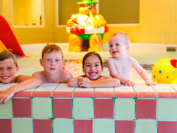 Vier blije jonge kinderen poseren en spelen in het ondiepe, kleurrijke kinderbad van Landal Wirfttal met een Bollo speelfiguur.