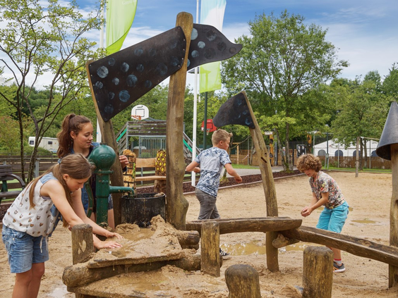 Kinderen spelen met een waterpomp en zand in de houten zand- en waterspeeltuin op vakantiepark Landal Wirfttal.