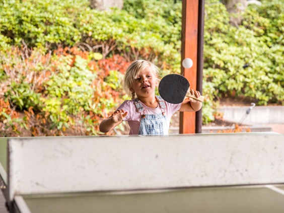 Een meisje speelt fanatiek een potje tafeltennis op de buitentafeltennistafel van Landgoed de Scheleberg.