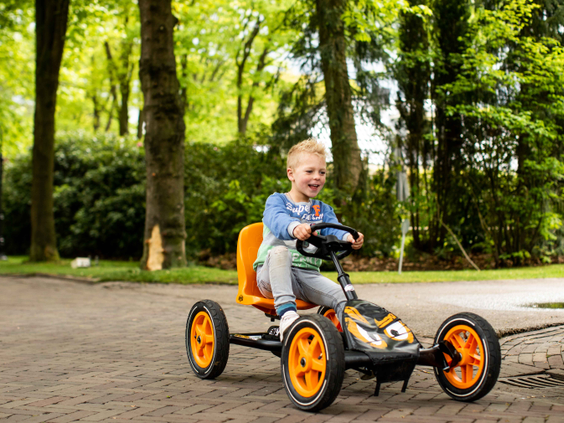 Een lachende jongen rijdt op een oranje skelter over een pad op vakantiepark Landgoed de Scheleberg, omgeven door bomen.
