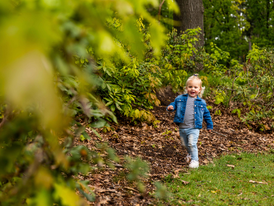 Een jong kind in een spijkerjasje rent lachend door de groene bossen van de Veluwe op Landgoed de Scheleberg.