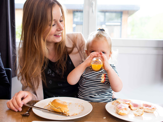 Een moeder zit gezellig met haar kindje aan tafel in het restaurant van Landgoed de Scheleberg, terwijl het kindje sap drinkt.