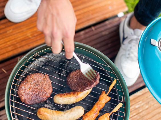 Close-up van hamburgers, worstjes en saté die liggen te garen op de hete grill van een barbecue bij een vakantiehuis.