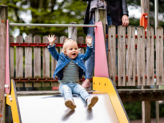 Een blij kind met de armen in de lucht glijdt van de glijbaan in de speeltuin van vakantiepark Landgoed de Scheleberg.