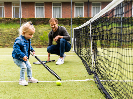 Een vader leert zijn jonge dochter tennissen op de all-weather tennisbaan van Landgoed de Scheleberg op de Veluwe.