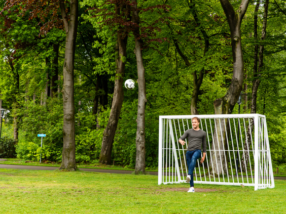 Een man trapt een voetbal richting het doel op het groene sportveld midden in de bossen van Landgoed de Scheleberg.