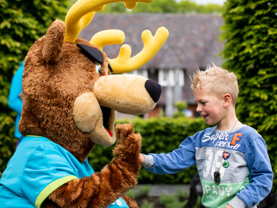 Een lachende jongen geeft een high five aan de grote poot van parkmascotte Spot op vakantiepark Landgoed de Scheleberg.