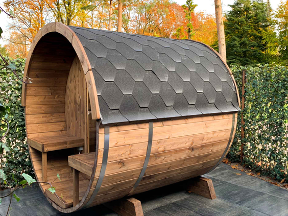 Een houten barrelsauna staat in de tuin van een wellness vakantiewoning op Landgoed de Scheleberg, klaar voor gebruik.