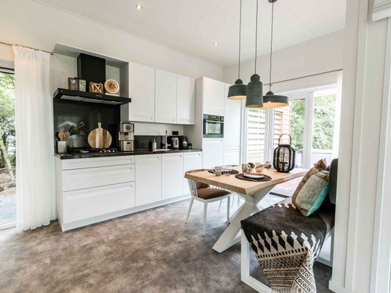 Interieur van een modern vakantiehuis met een witte, volledig uitgeruste keuken en een gezellige eethoek met houten tafel.