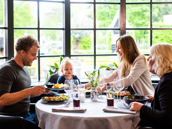 Een familie, inclusief een baby, geniet van een maaltijd aan een ronde tafel in het sfeervolle restaurant van Landgoed de Scheleberg.