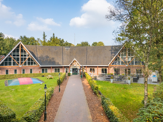 Het sfeervolle hoofdgebouw van vakantiepark Landgoed het Grote Zand in Drenthe, met op het grasveld een grote airtrampoline.