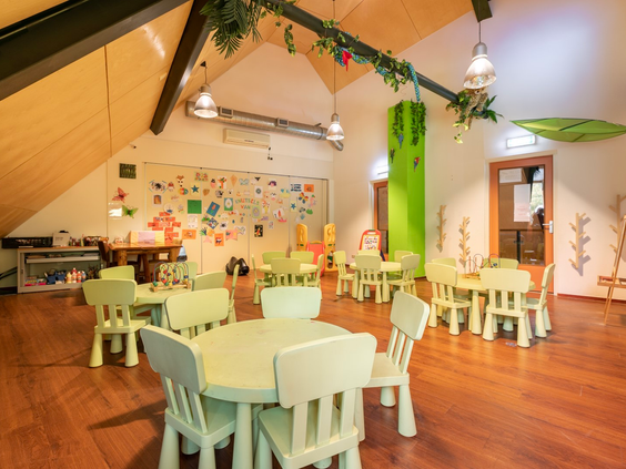 Een lichte speelhoek met kleine, witte kindertafels en -stoeltjes, waar de jongste kinderen rustig kunnen spelen of tekenen.