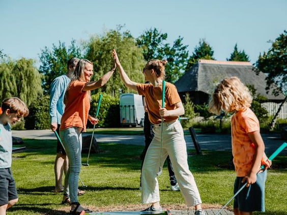 Een gezin speelt een actief buitenspel op een groot grasveld op Landgoed Ruwinkel en geeft elkaar een high five.