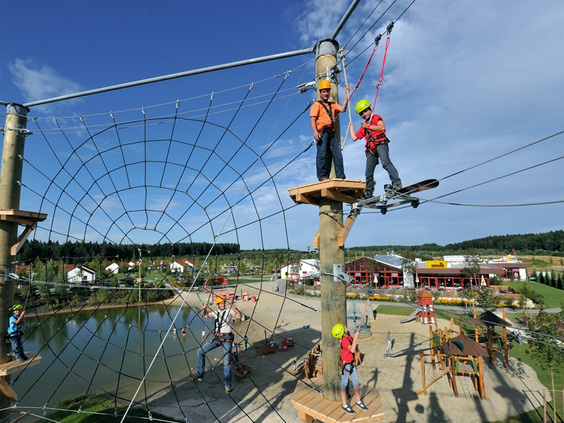 Kinderen met helmen op een spannend klimparcours hoog in de lucht in het vakantiepark van LEGOLAND Duitsland.