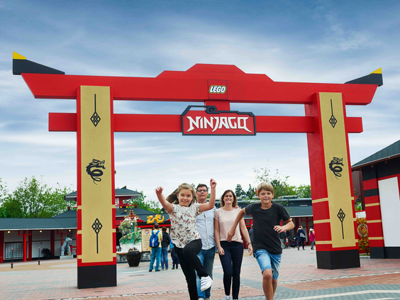 Gezin rent enthousiast door de poort van de LEGO NINJAGO World in attractiepark LEGOLAND Duitsland
