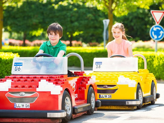 Kinderen rijden in rode en gele LEGO auto's bij de Hyundai Verkeersschool in LEGOLAND Duitsland en halen hun rijbewijs.