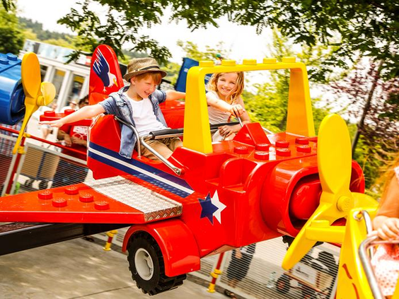 Lachende kinderen vliegen omhoog in een rode LEGO vliegtuig attractie in attractiepark LEGOLAND Duitsland.