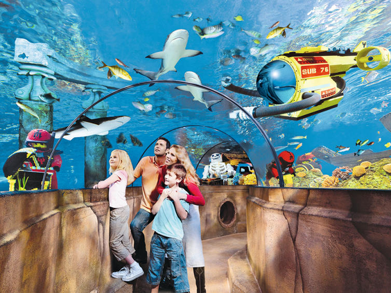 Gezin wandelt door de onderwatertunnel in LEGOLAND ATLANTIS by SEA LIFE en kijkt naar haaien, roggen en een LEGO onderzeeër.