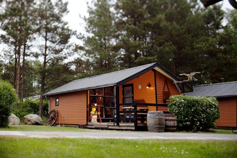 De buitenkant van een houten Wild West Cabin met veranda, gelegen in het groen van LEGOLAND Holiday Village.