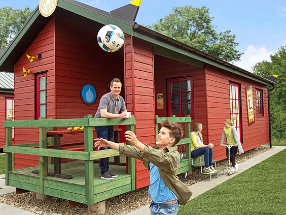 Een gezin dat aan het overgooien is met een bal voor hun rode vakantiehuisje in LEGOLAND Holiday Village.