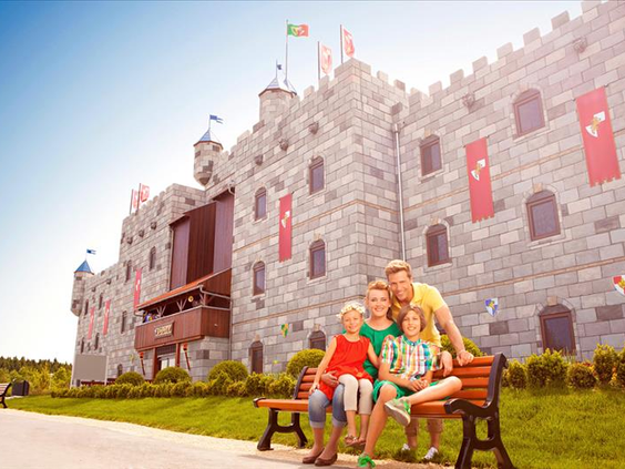 Een vrolijk gezin zittend op een bankje voor het indrukwekkende LEGO kasteelhotel (Königsburg) in het LEGOLAND Feriendorf in Beieren.