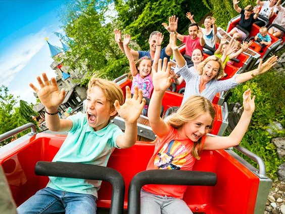 Lachende kinderen met hun handen in de lucht in een rode achtbaan-karretje tijdens een rit in attractiepark LEGOLAND Duitsland.