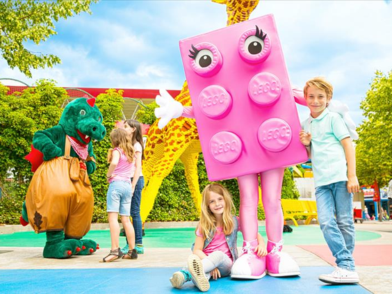 Kinderen poseren vrolijk met levensgrote LEGO figuren, waaronder een groene draak en een roze LEGO steen, in LEGOLAND Duitsland.