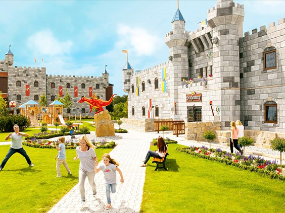 Kinderen spelen in de kasteeltuin van het LEGOLAND hotel, met op de voorgrond een grote rode LEGO draak en de kasteelgebouwen erachter.