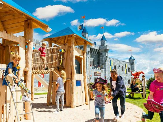 Kinderen, waaronder een meisje met een piratenhoed, spelen op een houten klimrek in de avontuurlijke speeltuin van het LEGOLAND Feriendorf.