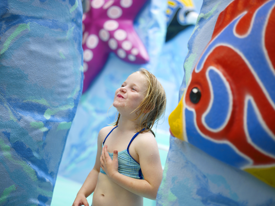 Een meisje geniet van het water dat uit een kleurrijke vis stroomt in het kinderbad van zwemparadijs Aqua Mundo in Limburgse Peel.