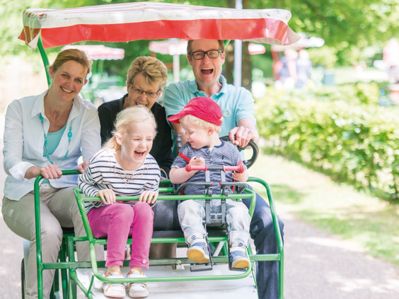 Een lachende familie met twee kinderen en grootouders maakt een ritje op een familiefiets in Center Parcs Limburgse Peel.