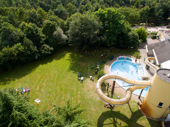 Een luchtfoto van de kronkelende waterglijbaan en het buitenbad van Center Parcs Limburgse Peel, omgeven door een groene ligweide