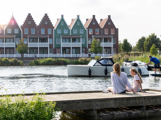 Een moeder en dochter genieten van het uitzicht over het water, zittend op een steiger met de typische Volendamse vakantiehuizen op de achtergrond.