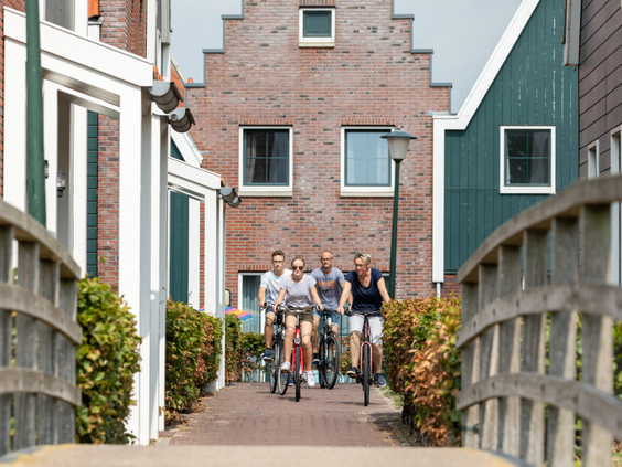 Een gezin fietst vrolijk over een bruggetje op Marinapark Volendam, langs de karakteristieke vakantiehuizen in Volendamse stijl.
