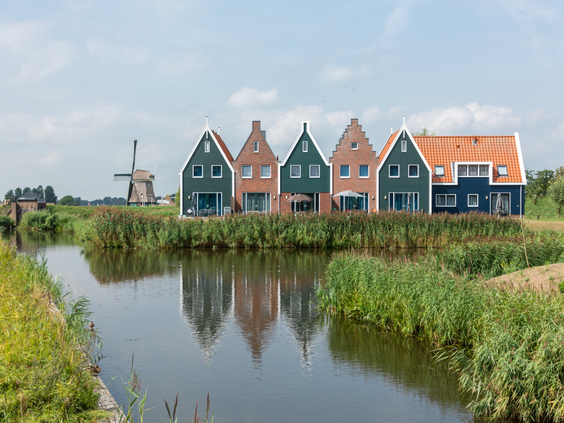 De kleurrijke vakantiehuizen van Marinapark Volendam weerspiegelen in het water, met in de verte een klassieke Hollandse windmolen.