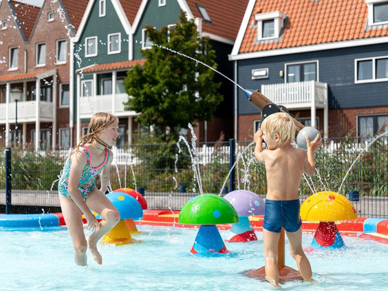 Twee kinderen spelen en spetteren vrolijk in het ondiepe kinderbad met kleurrijke fonteintjes en speelelementen.