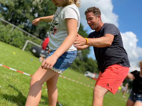 Een vader helpt zijn dochter met een spelletje of activiteit op een groot grasveld op Marveld Recreatie.