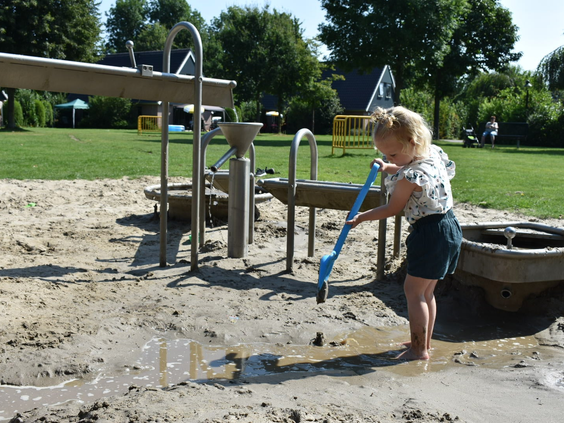 Een kind is met een schep en een waterpomp aan het spelen in de water- en zandspeeltuin van Marveld Recreatie.