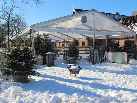 Een besneeuwd terras in de winter op Marveld Recreatie, sfeervol aangekleed met kerstbomen en vuurkorven.