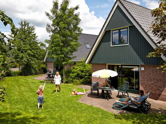 Gezin geniet van de ruime tuin bij een luxe vakantiewoning op Marveld Recreatie, met spelende kinderen en ouders op het terras.
