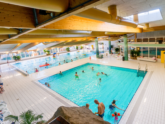 Overzicht van het grote subtropische binnenzwembad van Marveld Recreatie vol met zwemmende kinderen en families.