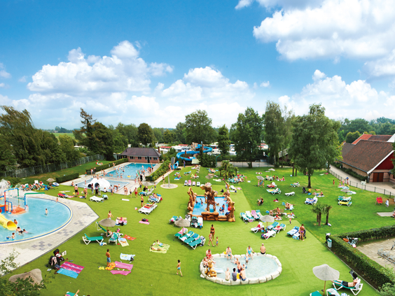 Grote, groene ligweide vol met families en kinderen die zonnen en spelen bij het buitenzwembad van Marveld Recreatie.