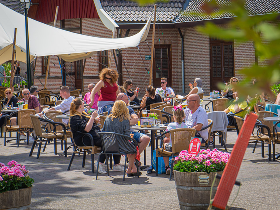 Een gezellig, vol terras bij een van de horecagelegenheden op Marveld Recreatie waar gasten genieten van een drankje.