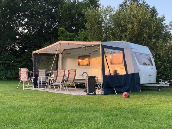 Een caravan met voortent staat op een ruime en groene kampeerplek op de camping van Marveld Recreatie.
